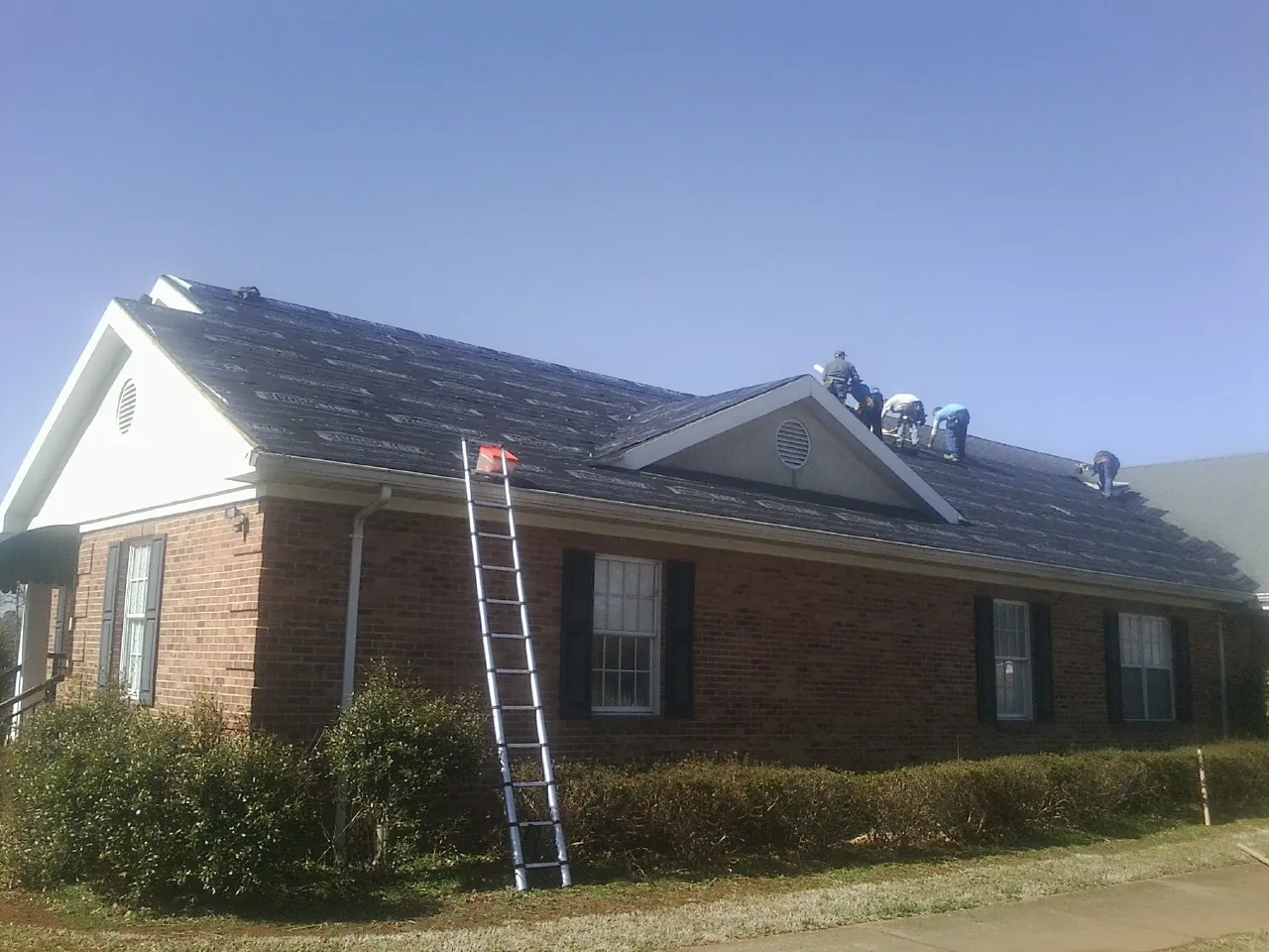 Crew tearing shingles off a brick ranch roof with a ladder set — Emergency Roof Repair work by our crew in Bow