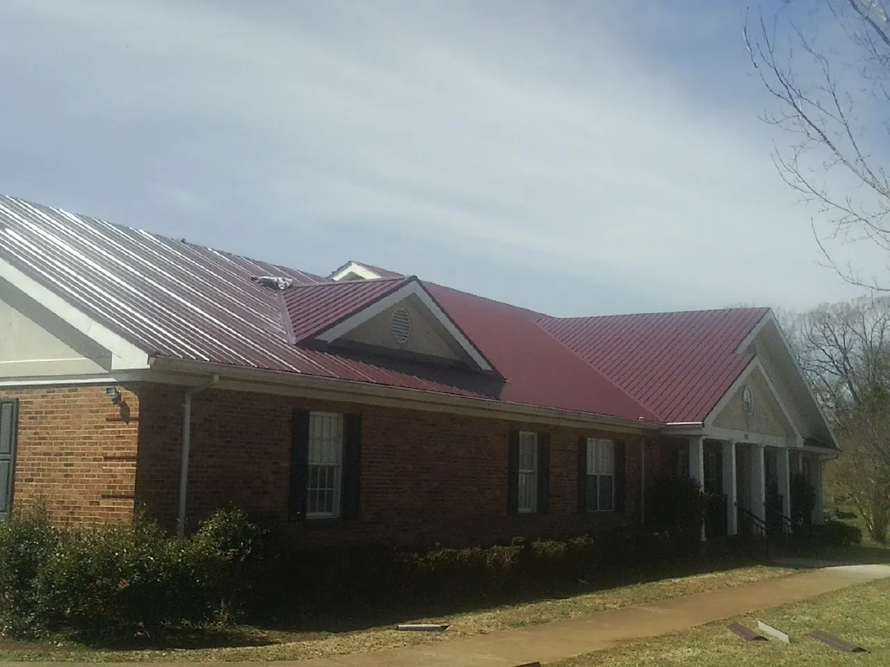 Red metal roof with gabled entries on a long brick building, from a Hail Damage Roof Repair job in Bow