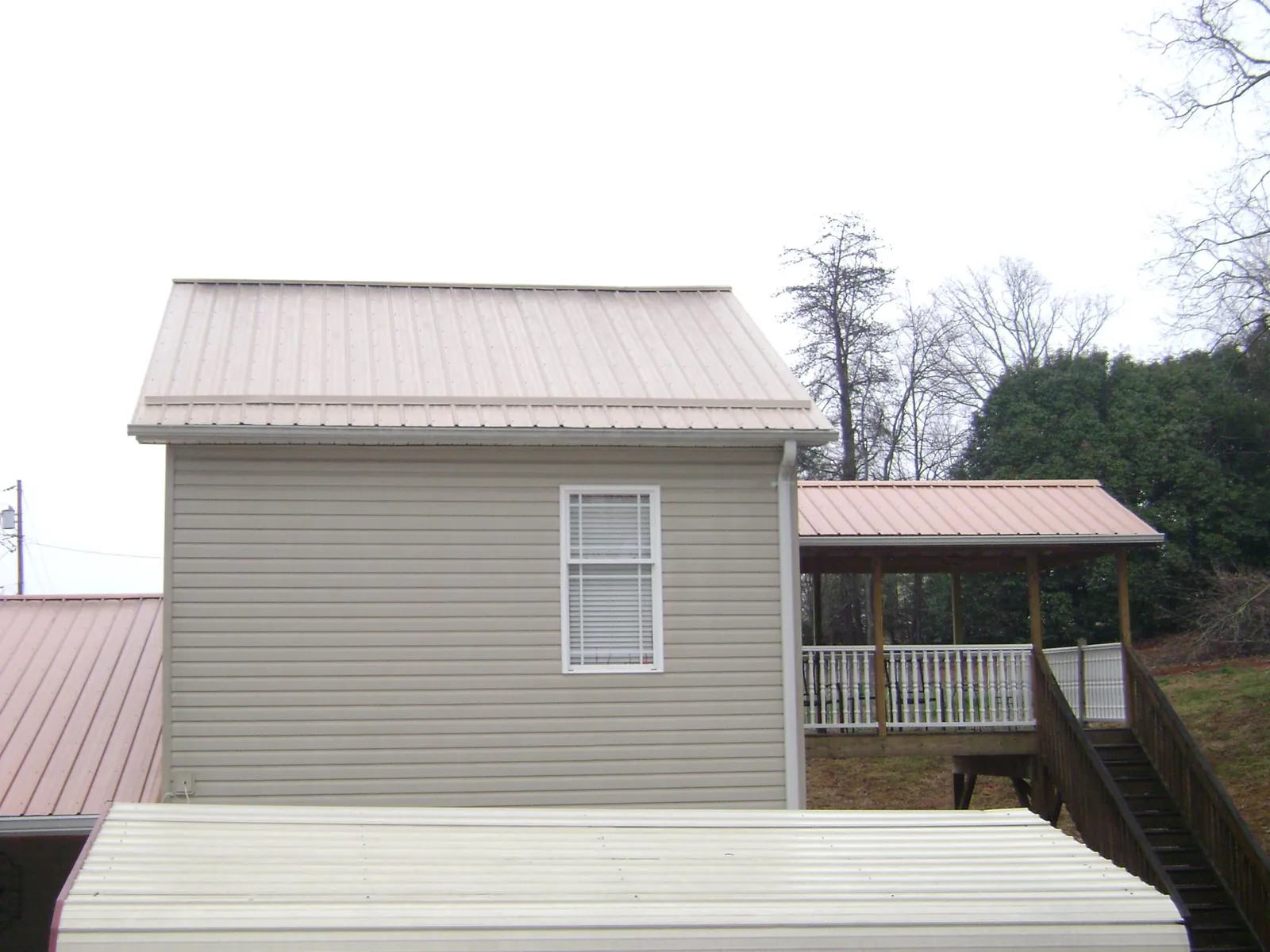 Tan metal roofs on a two story addition and attached porch, from a Roof Replacement job in Bow